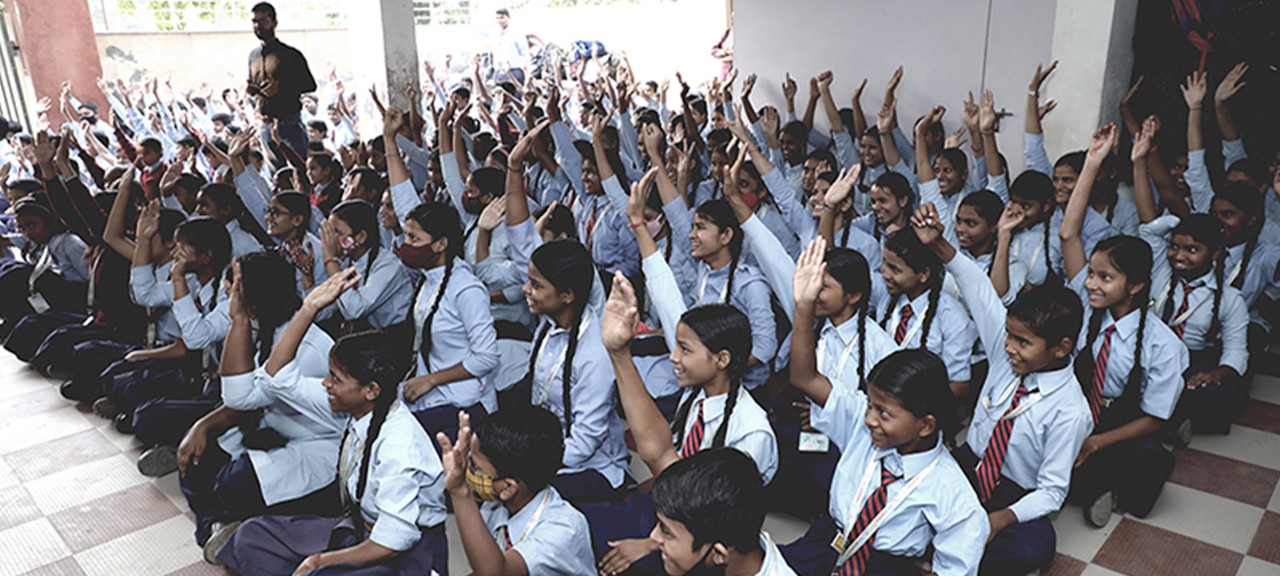 Indian students smiling and raising their hands as they participate in a health camp led by Boston Scientific employees. 