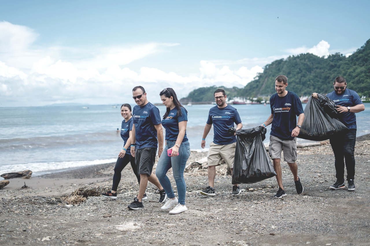 Group of six Boston Scientific employees walk down a beach while picking up trash. 