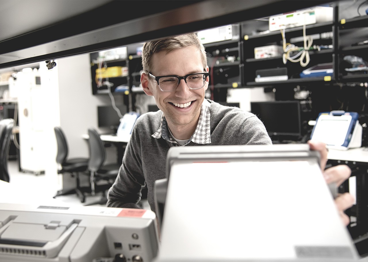 Man wearing glasses smiles while looking at a monitor.