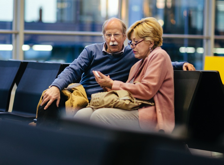 Older husband and wife in the airport looking at a mobile device