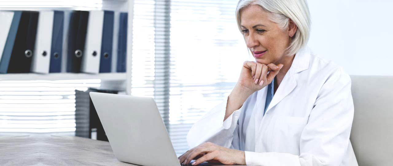 doctor in white lab coat looking at laptop screen on desk